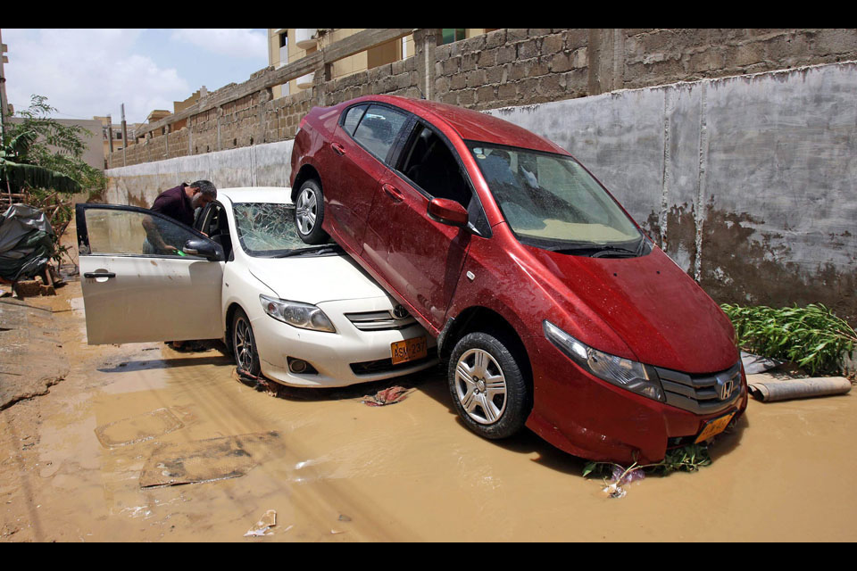 People check their damaged vehicles following torrential rains in Karachi
