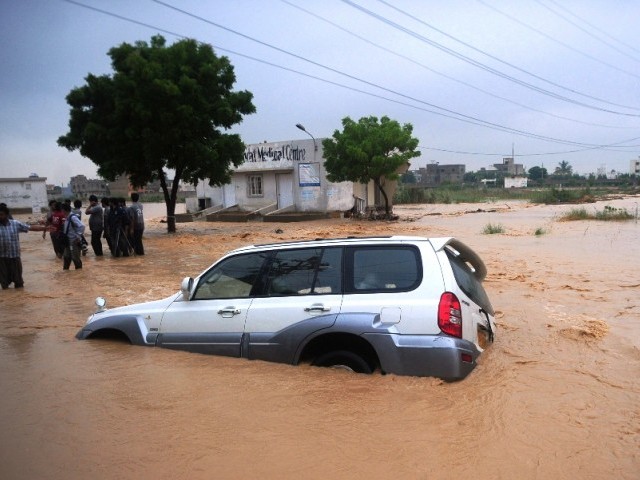 Residents stand near a partially submerged vehicle as they evacuate a flooded area in Karachi